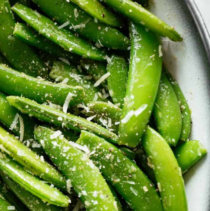 Cacio E Pepe Sugar Snap Peas served in a white bowl with a black rim. Garnished with extra parmesan cheese and cracked black pepper. | craveitall.com