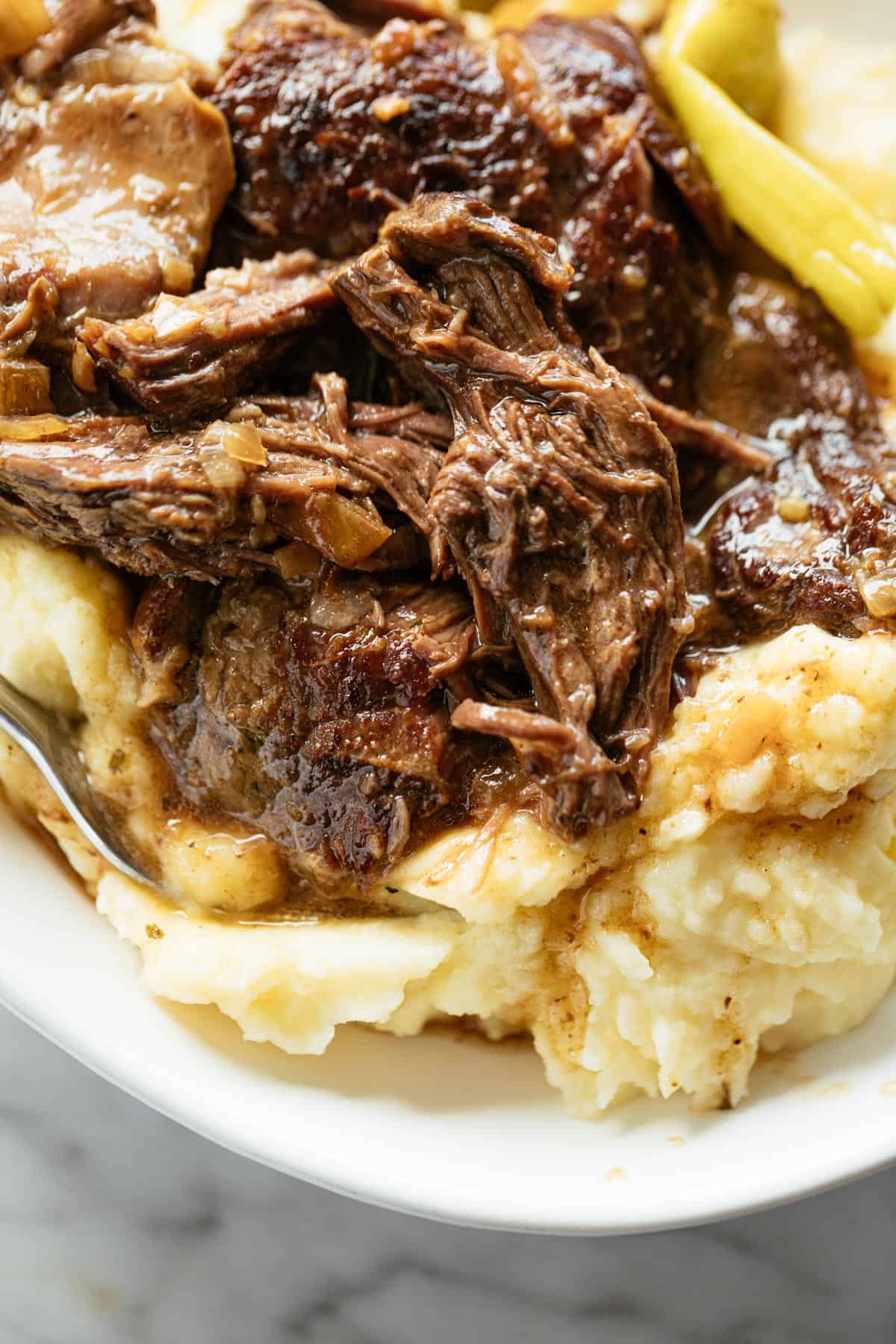Mississippi Pot Roast shredded into pieces and served in a white bowl over mashed potatoes. | craveitall.com