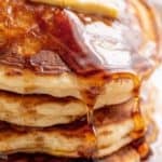 A stack of Fluffy Pancakes on a white plate served with butter and drizzled with maple syrup. | craveitall.com