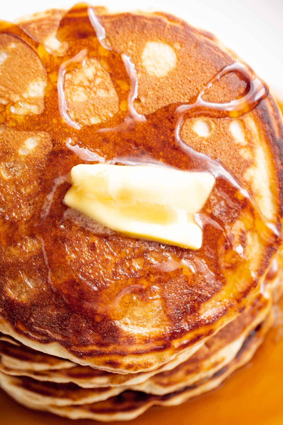 A stack of Fluffy Pancakes on a white plate served with butter and drizzled with maple syrup. | craveitall.com